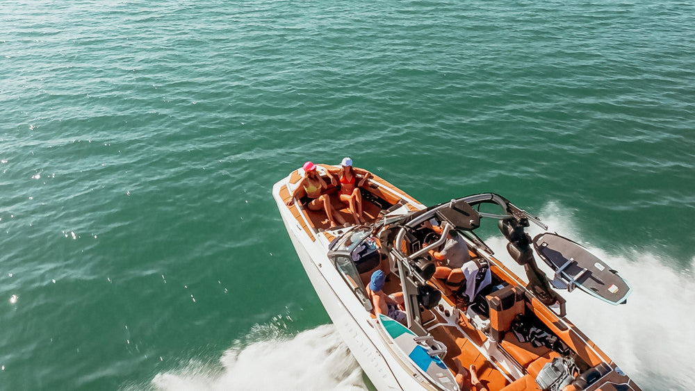 An aerial view captures several friends enjoying a sunny day on a speed boat, cruising through turquoise waters with water sports gear.