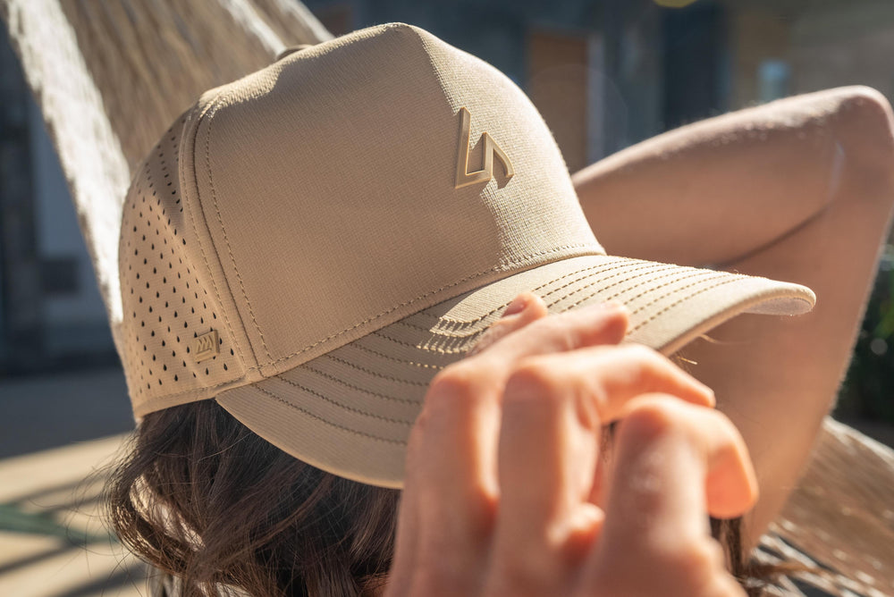 A person wearing a beige Suay Apex cap with mesh panels relaxes outdoors, hand gently resting near the brim.