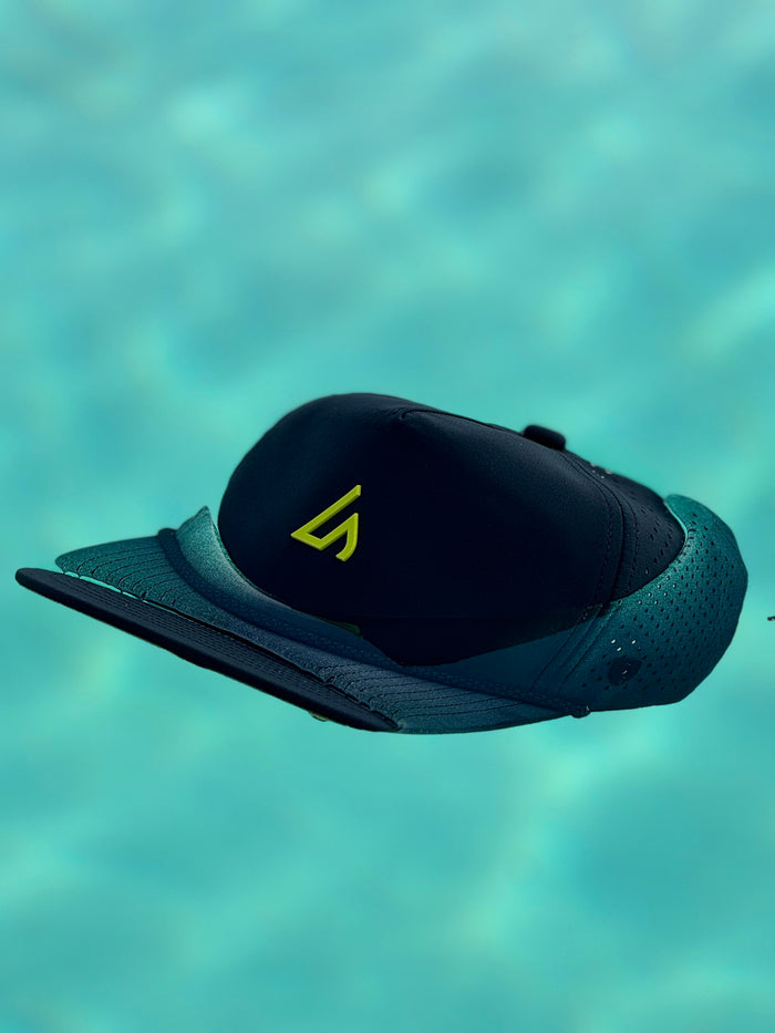 A dark navy Apex cap with a bright yellow Suay logo floats serenely on clear turquoise water, showcasing its design and water-friendly nature.