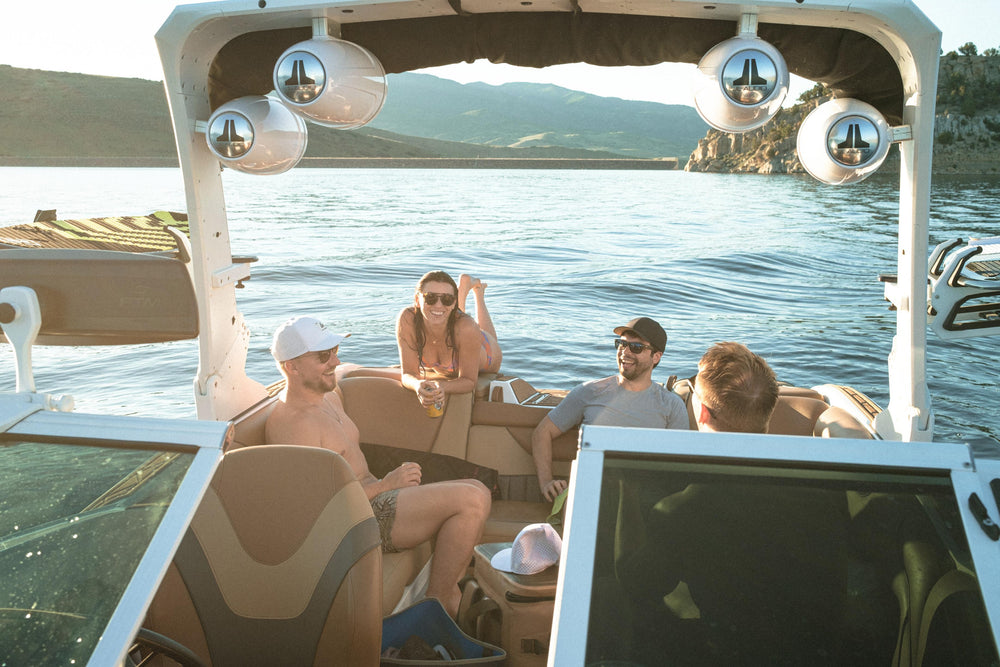 Four friends enjoy a relaxed golden hour boat ride on a scenic lake, with one man prominently wearing a white Suay Apex hat.