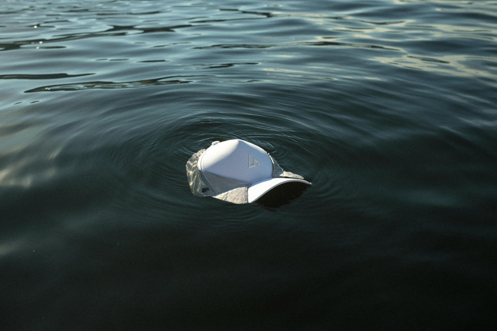 A pristine white Suay Apex hat floats serenely on the dark, rippling surface of water, creating a clean and adventurous aesthetic.