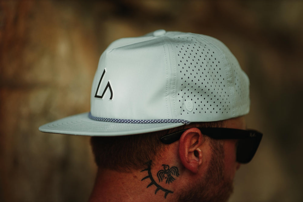 A person wears a light mint Suay Drift hat with a flat brim and rope detail, featuring the 'LS' logo and perforated panels, against a blurred outdoor background.